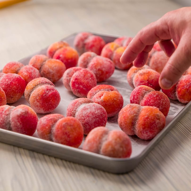 A hand reaching for a tray of Cafe Balkan's peach-shaped, sugar-dusted pastries.