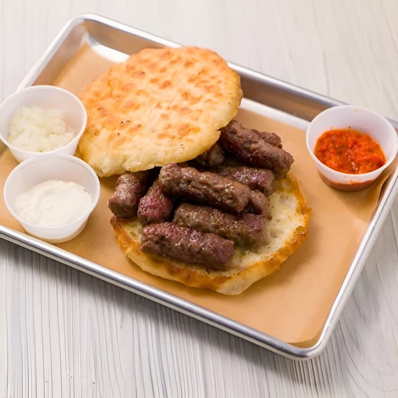 Cafe Balkan's cevapi, a European dish, with flatbread, chopped onions, sour cream, and red pepper sauce.