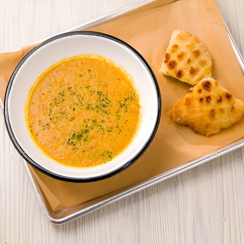A bowl of creamy orange soup with herbs and two pieces of baked bread on a tray.