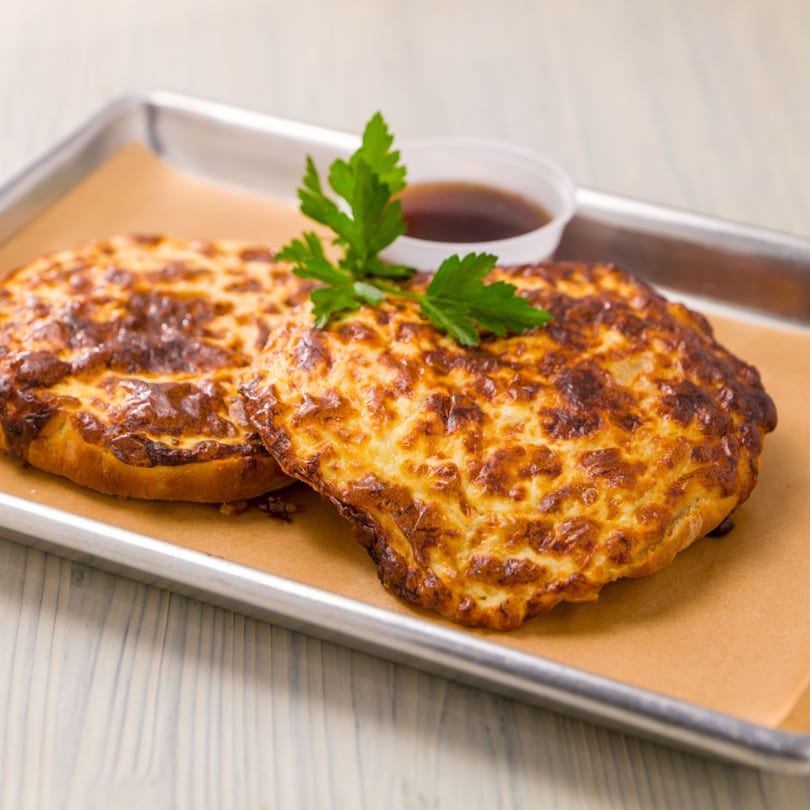 Two golden-brown cheese pastries with parsley garnish and a side of dipping sauce on a tray.