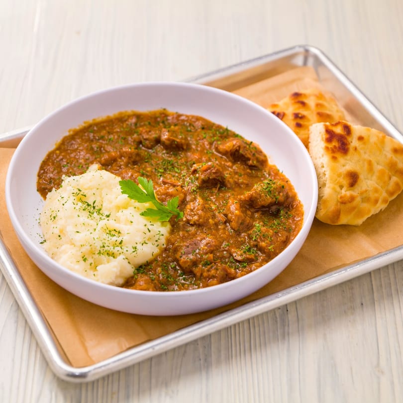 Cafe Balkan's goulash with mashed potatoes and flatbread on a metal tray.